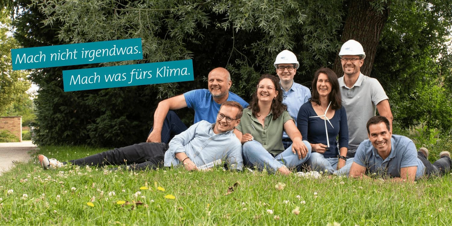 Sieben Personen sitzen nebeneinander auf einer Wiese, im Hintergrund Bäume. Links im Bild der Slogan: 'Mach nicht irgendwas. Mach was fürs Klima'!